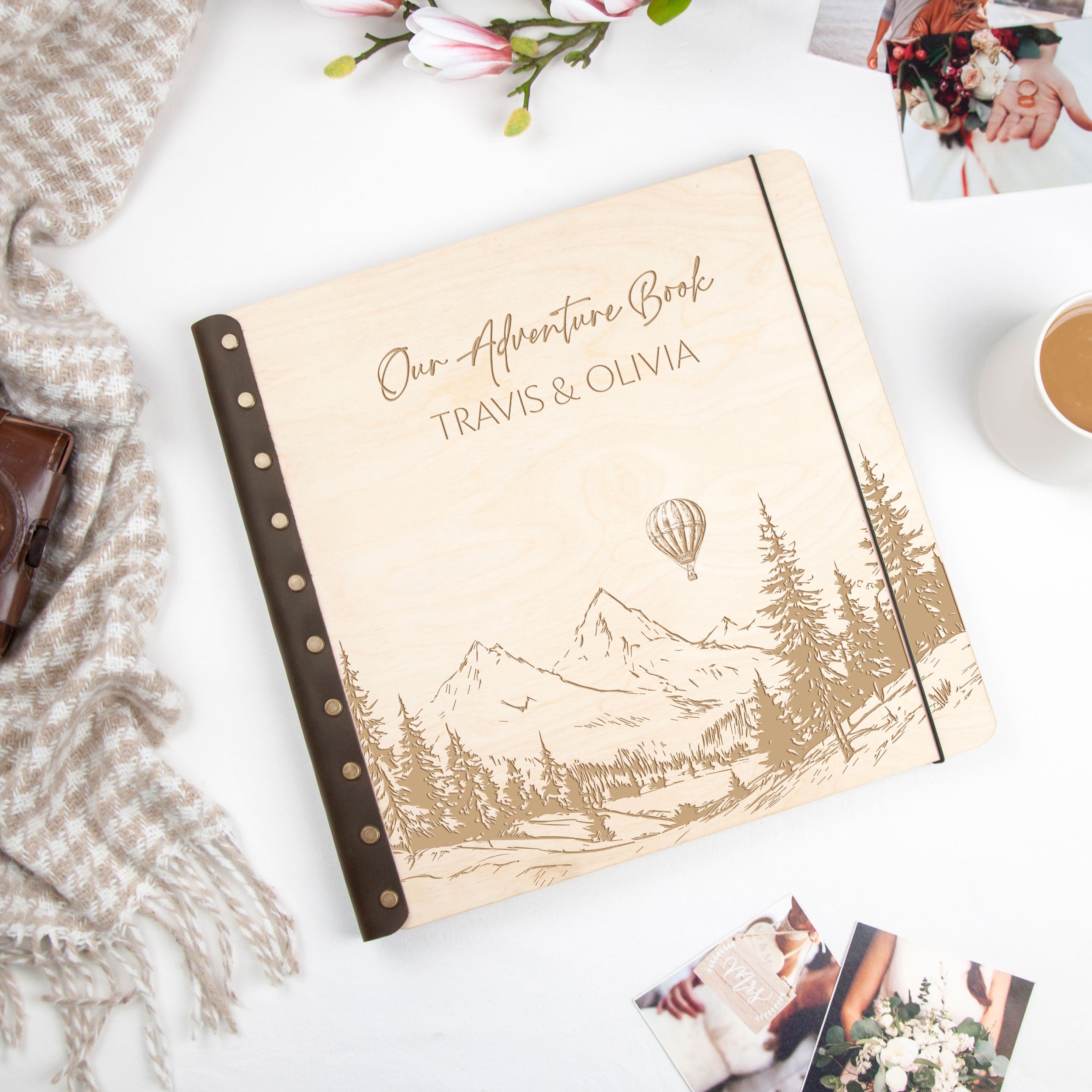 a wooden book with a mountain landscape and a hot air balloon on the cover, along with some photographs and a cup of coffee.