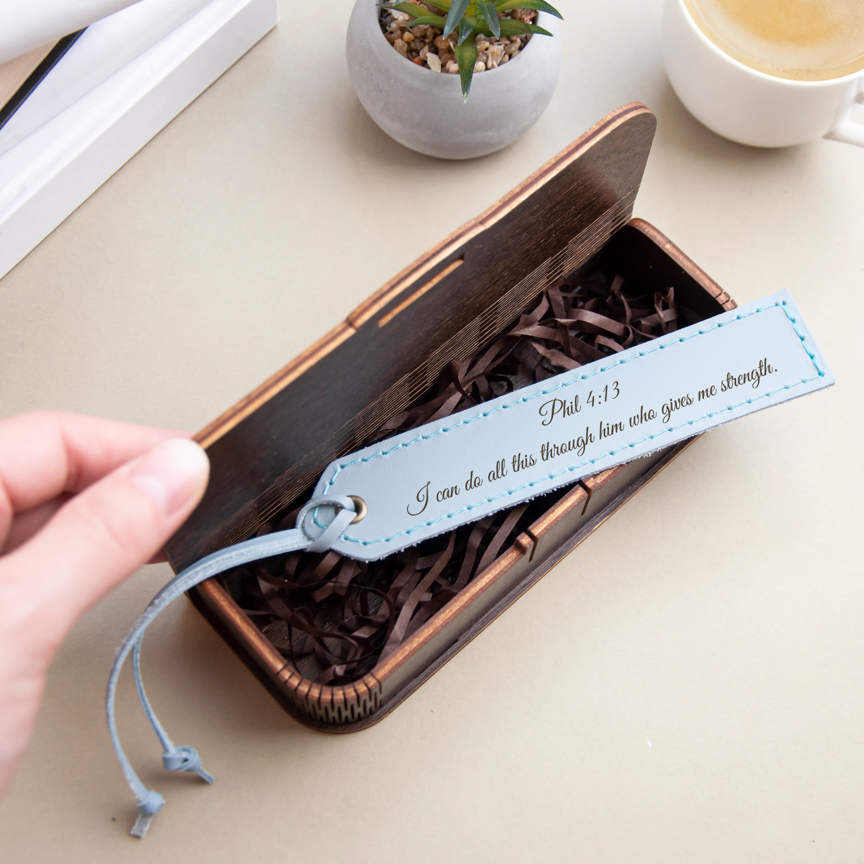 A wooden box with a blue tag attached, containing brown shredded paper, and a hand is reaching into the box.
