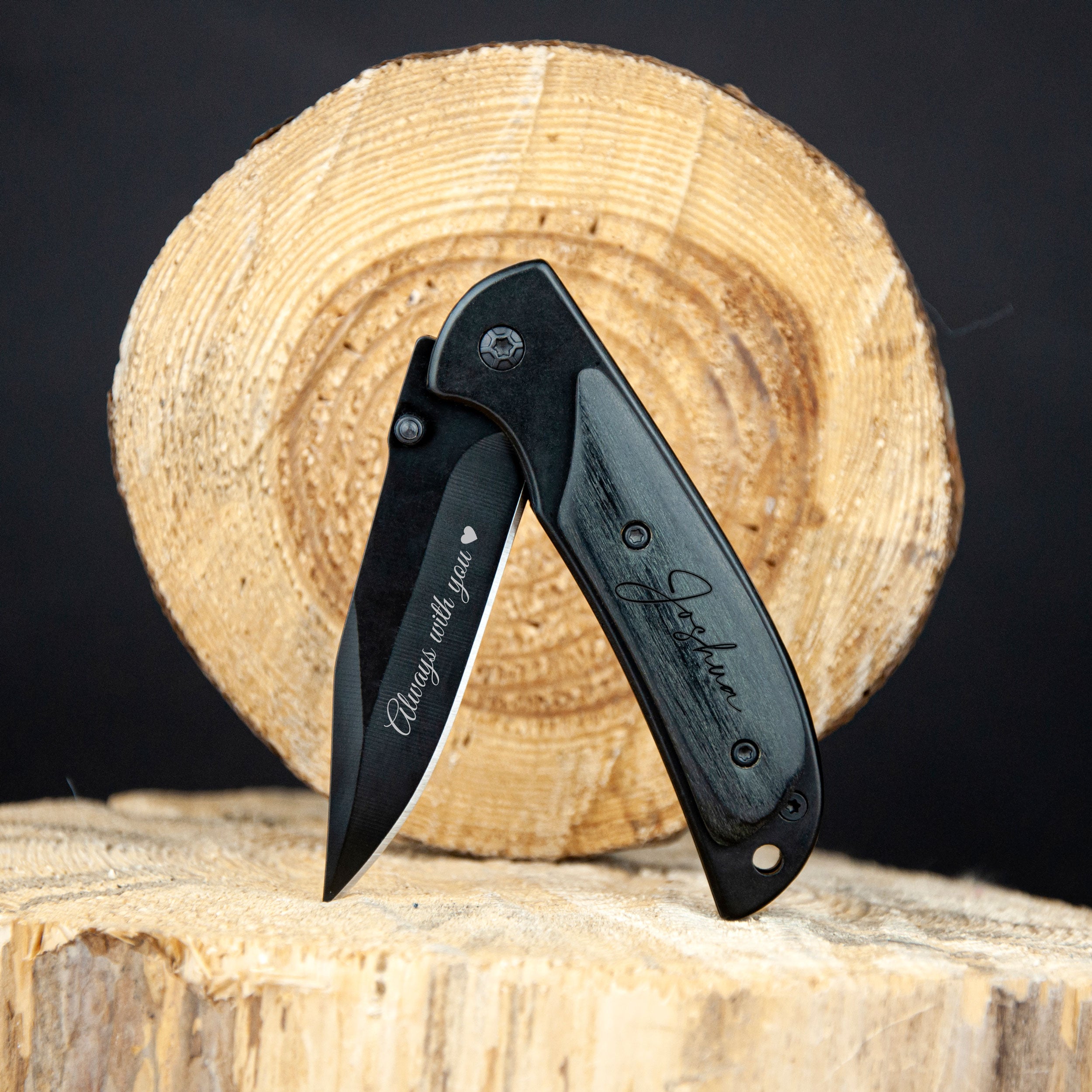 A black pocket knife with a wooden handle is placed on a wooden log, with the blade facing upwards.