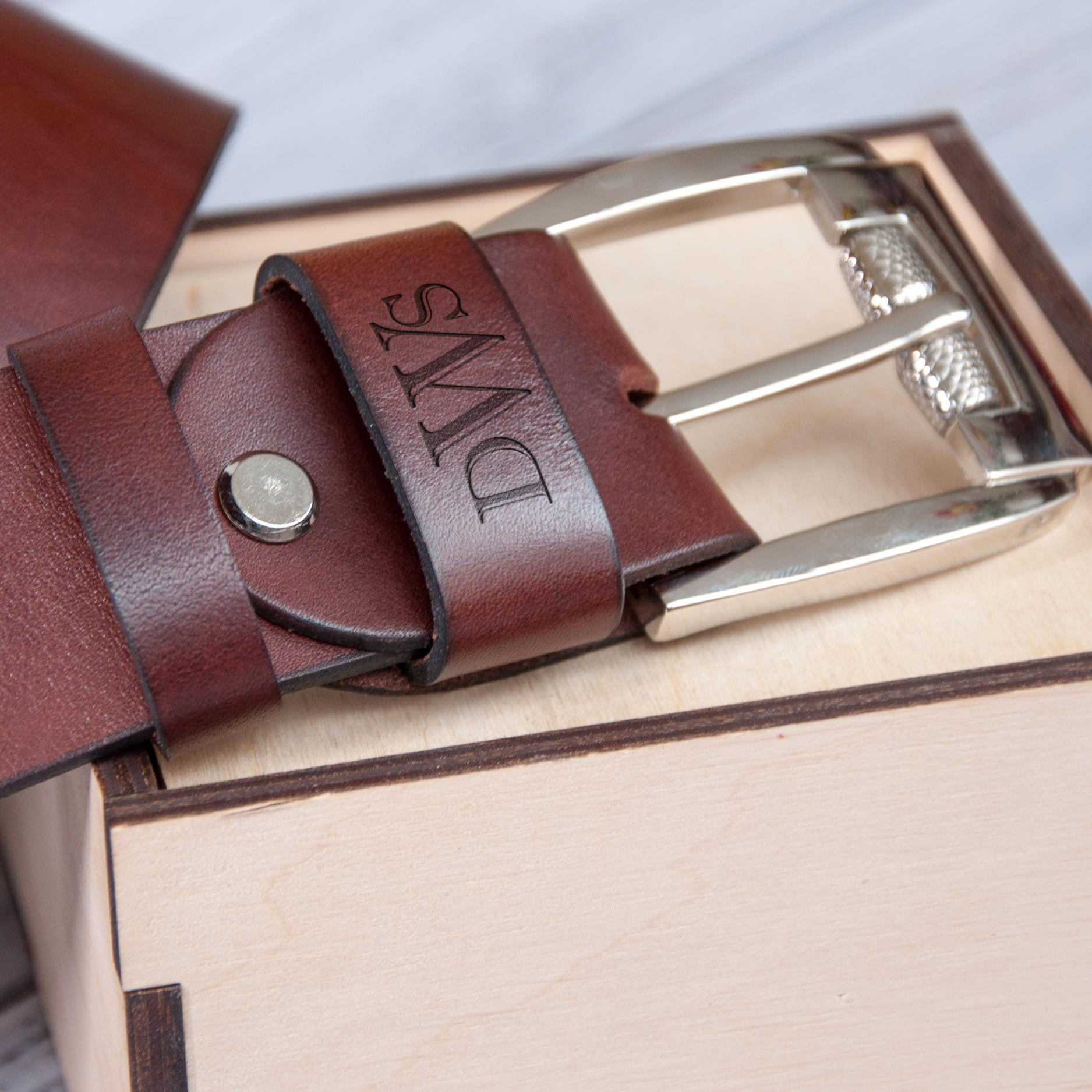 A brown leather belt with a silver buckle is placed on a wooden surface.