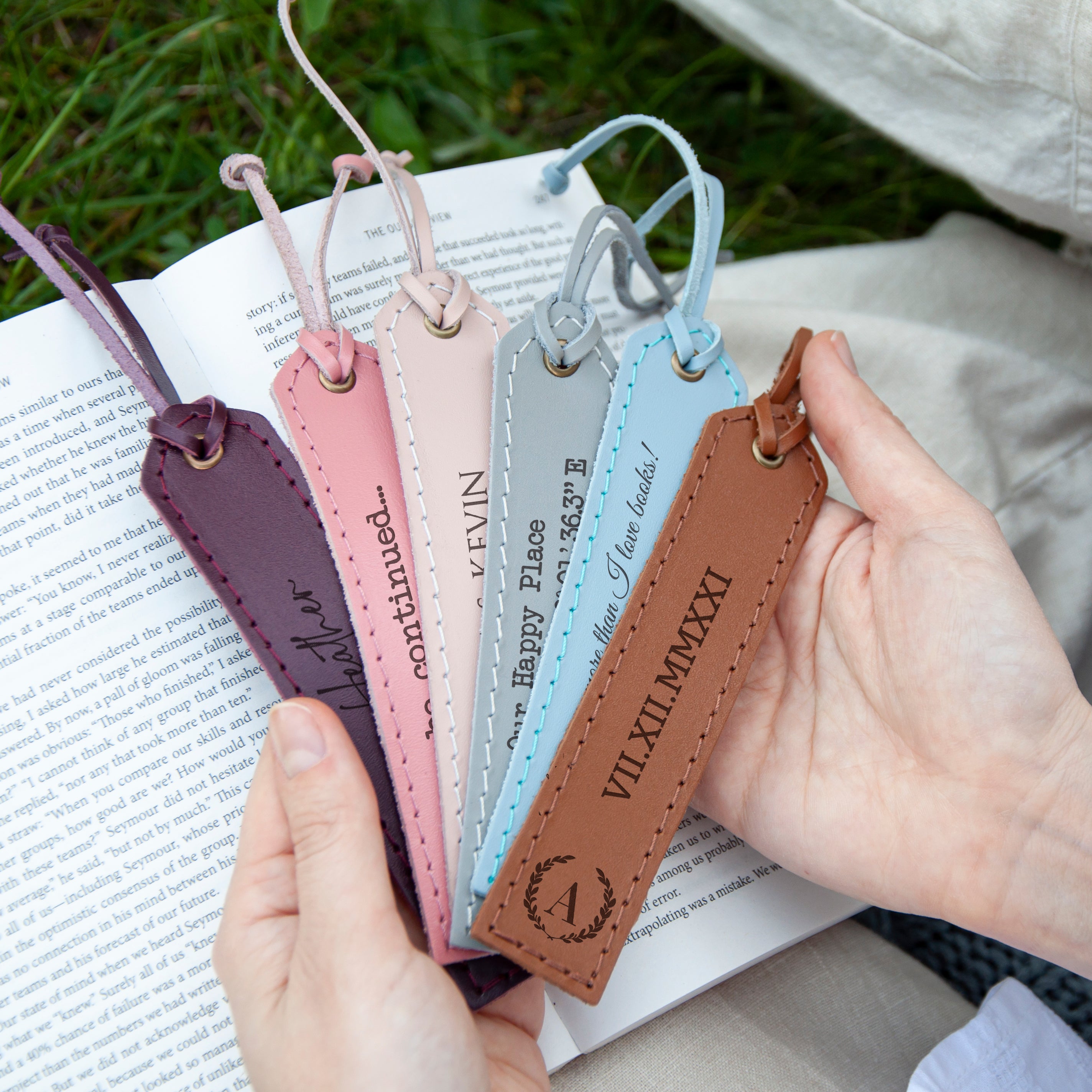 A person's hands holding a book with a row of colorful leather bookmarks attached to the pages.