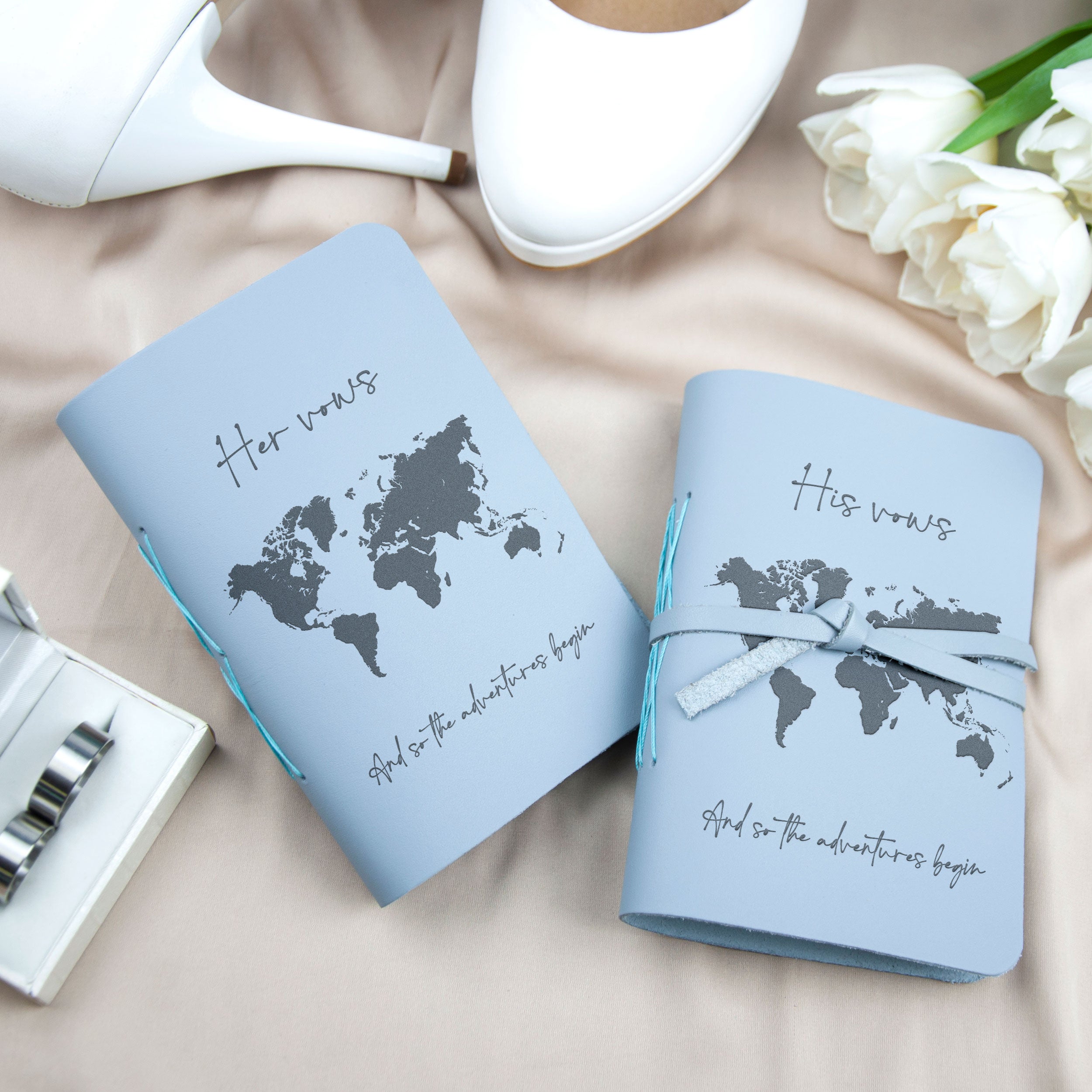 two blue notebooks with a world map design, along with a pair of white high heels and a bouquet of white roses.