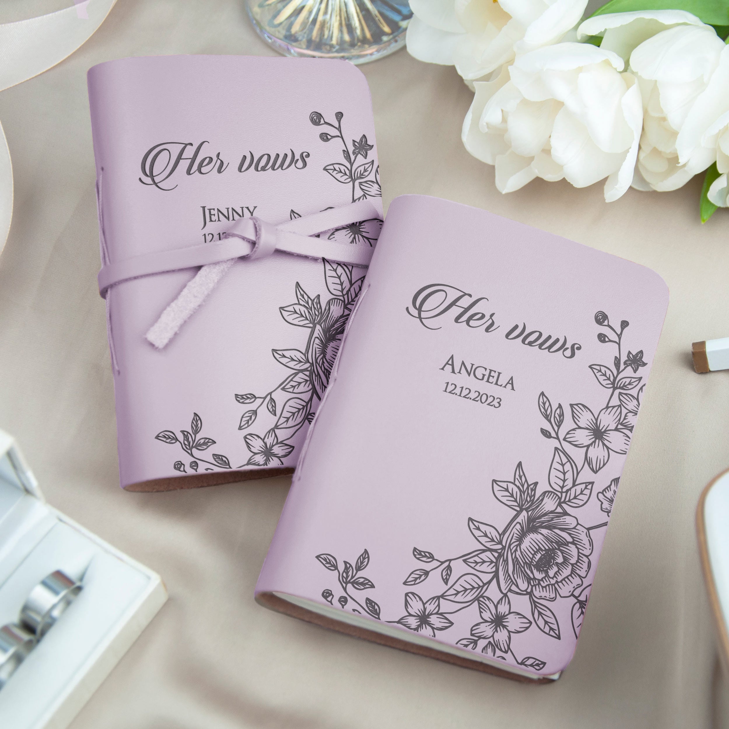 two personalized wedding vows books with floral designs, placed on a table with white flowers in the background.