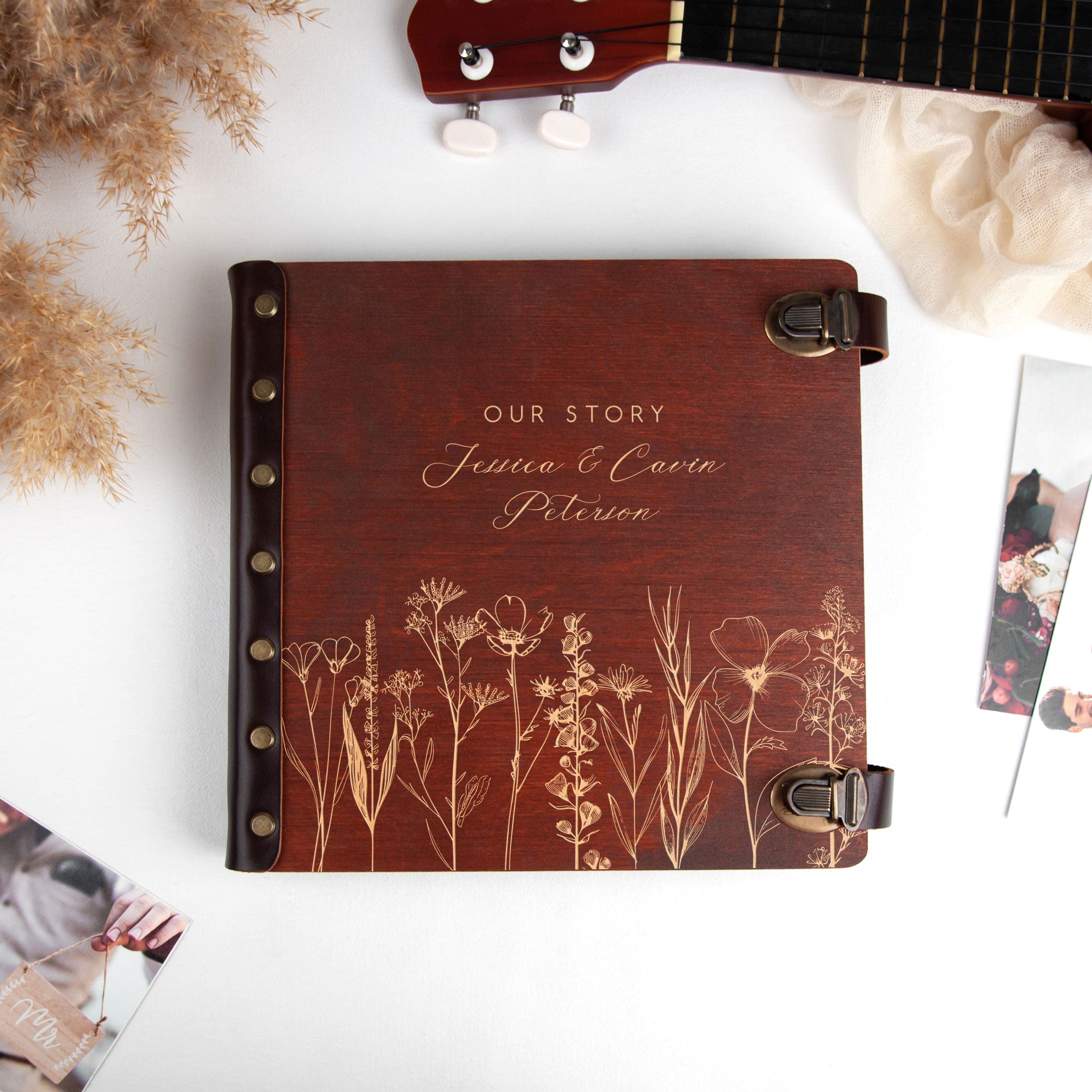 A wooden photo album with the text "OUR STORY" and the names "Jenna & cabin Peterson" printed on it, along with a guitar and other personal items.