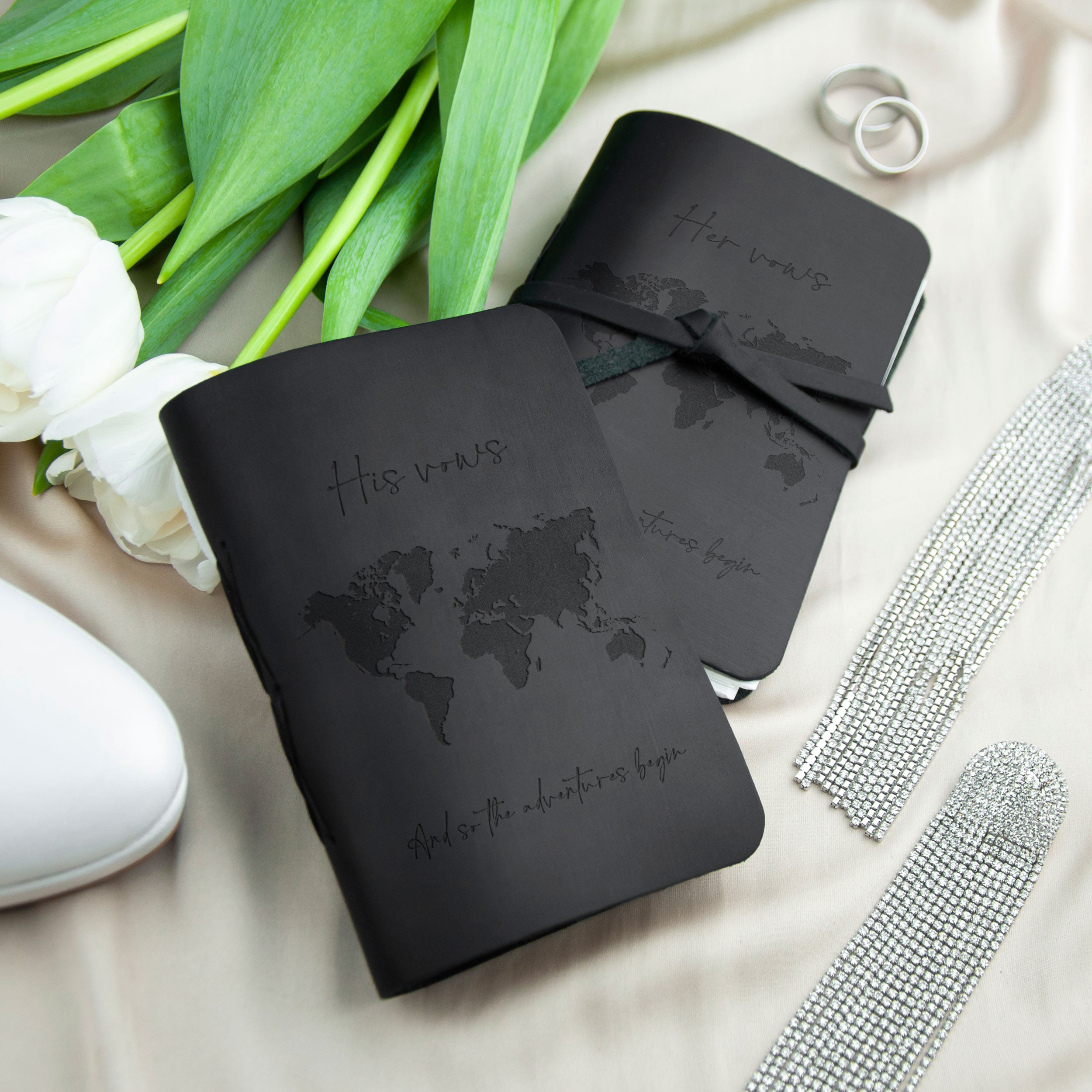 a black book with a world map on the cover, along with a silver ring and a silver bracelet, all placed on a white surface.