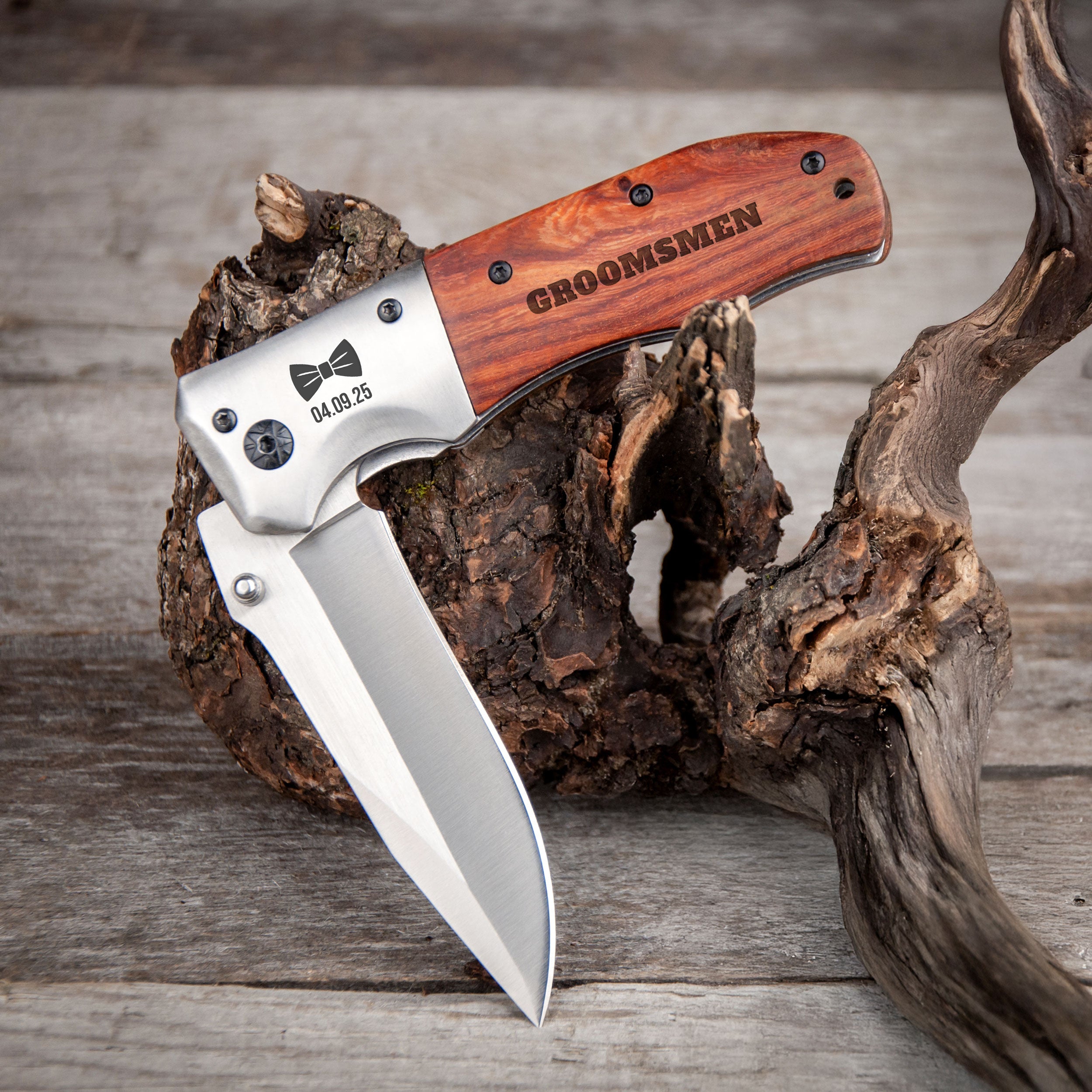 A knife with a wooden handle and engraved text is resting on a piece of driftwood on a wooden surface.