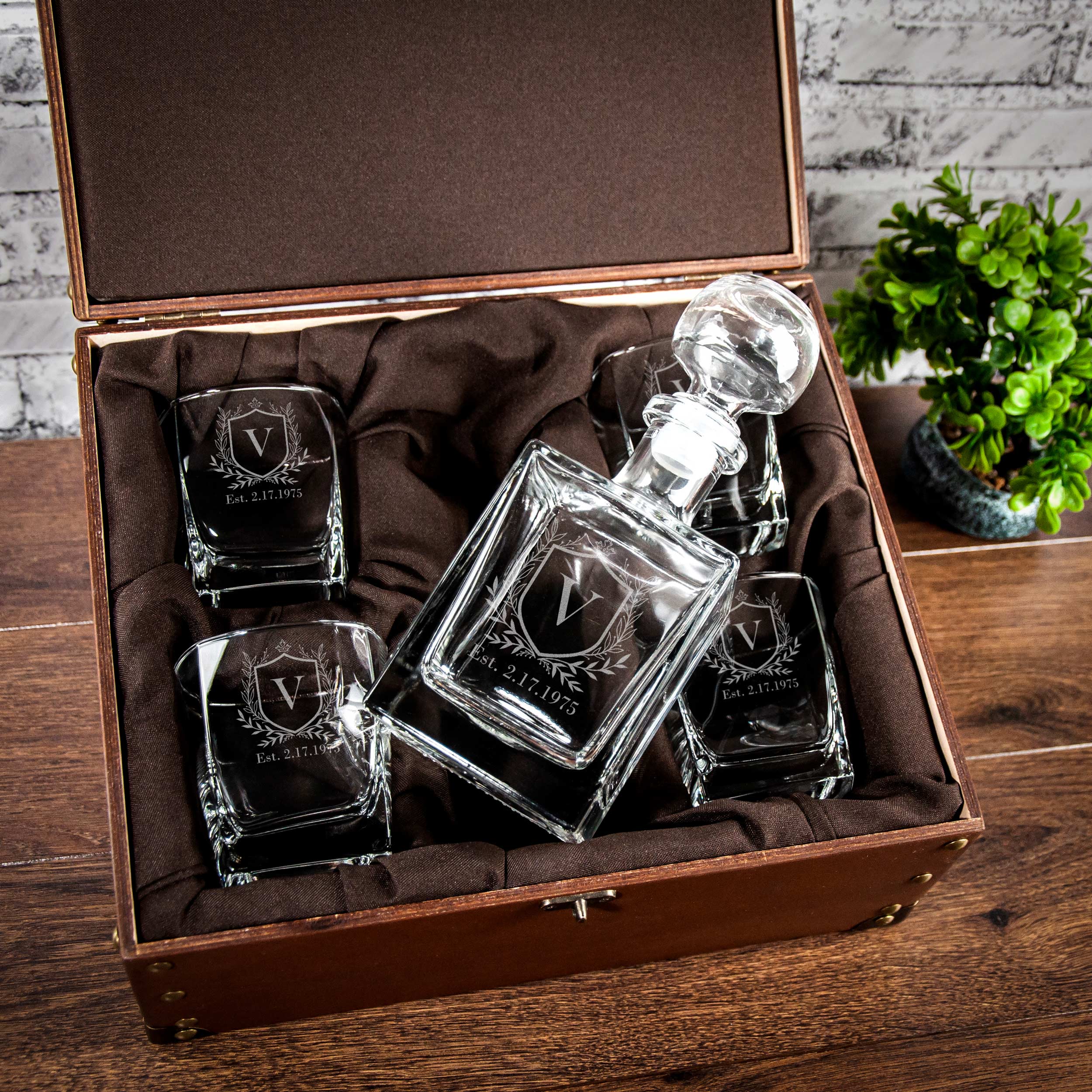 A set of four clear glass decanters and four matching glasses are displayed in a brown wooden box, placed on a wooden surface.