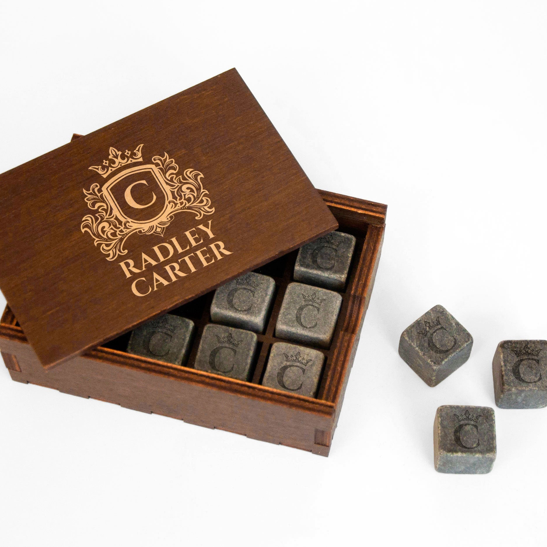 A wooden box with a lid, containing several gray stone cubes with a large "C" on them, and a few additional gray stone cubes on the side.