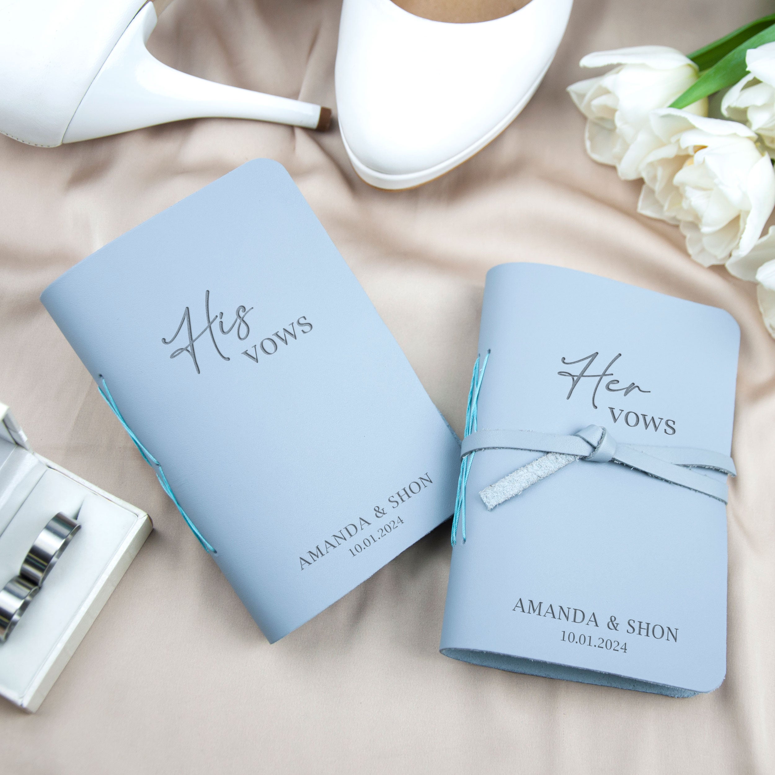 a pair of blue wedding vows books with the names 'Amanda & Shon' printed on them, along with a pair of white high heels and a bouquet of white roses.
