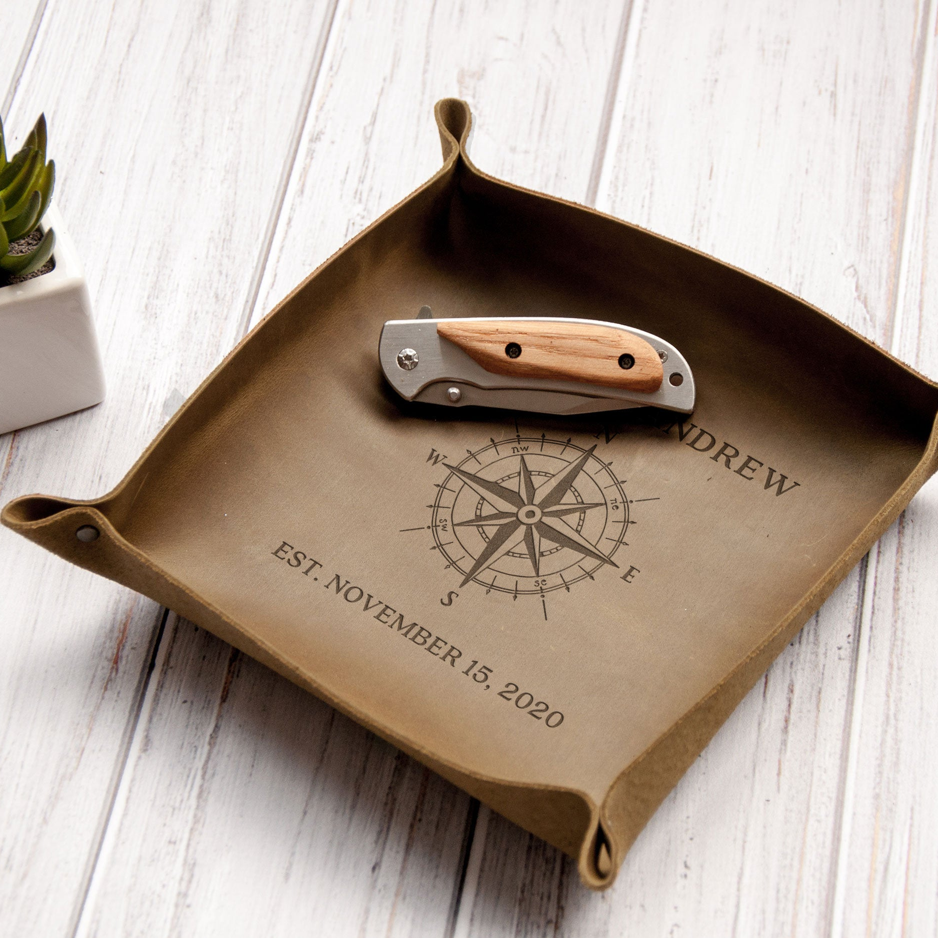 A brown leather tray with a compass design and the name "ANDREW" printed on it, along with the date "EST. NOVEMBER 15, 2020".