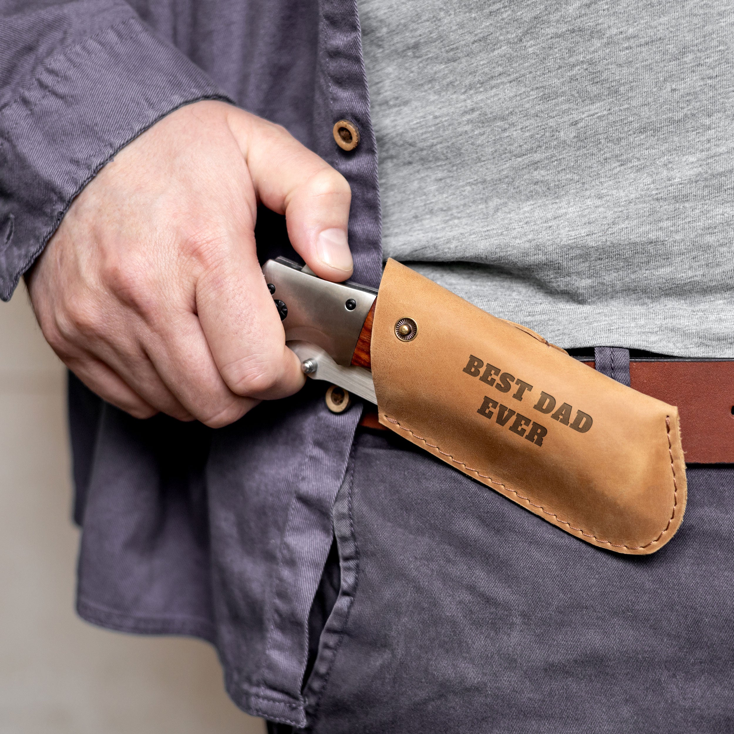A person's hand holding a knife with a leather pouch that says "Best Dad Ever".
