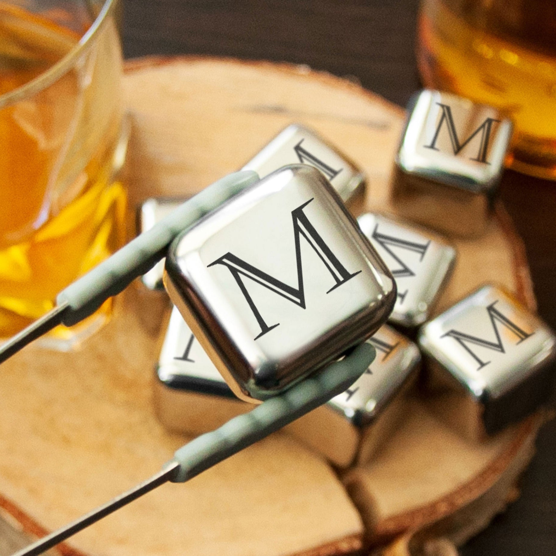 a close-up of a pair of tongs holding a metal cube with the letter "M" on it, surrounded by other metal cubes.