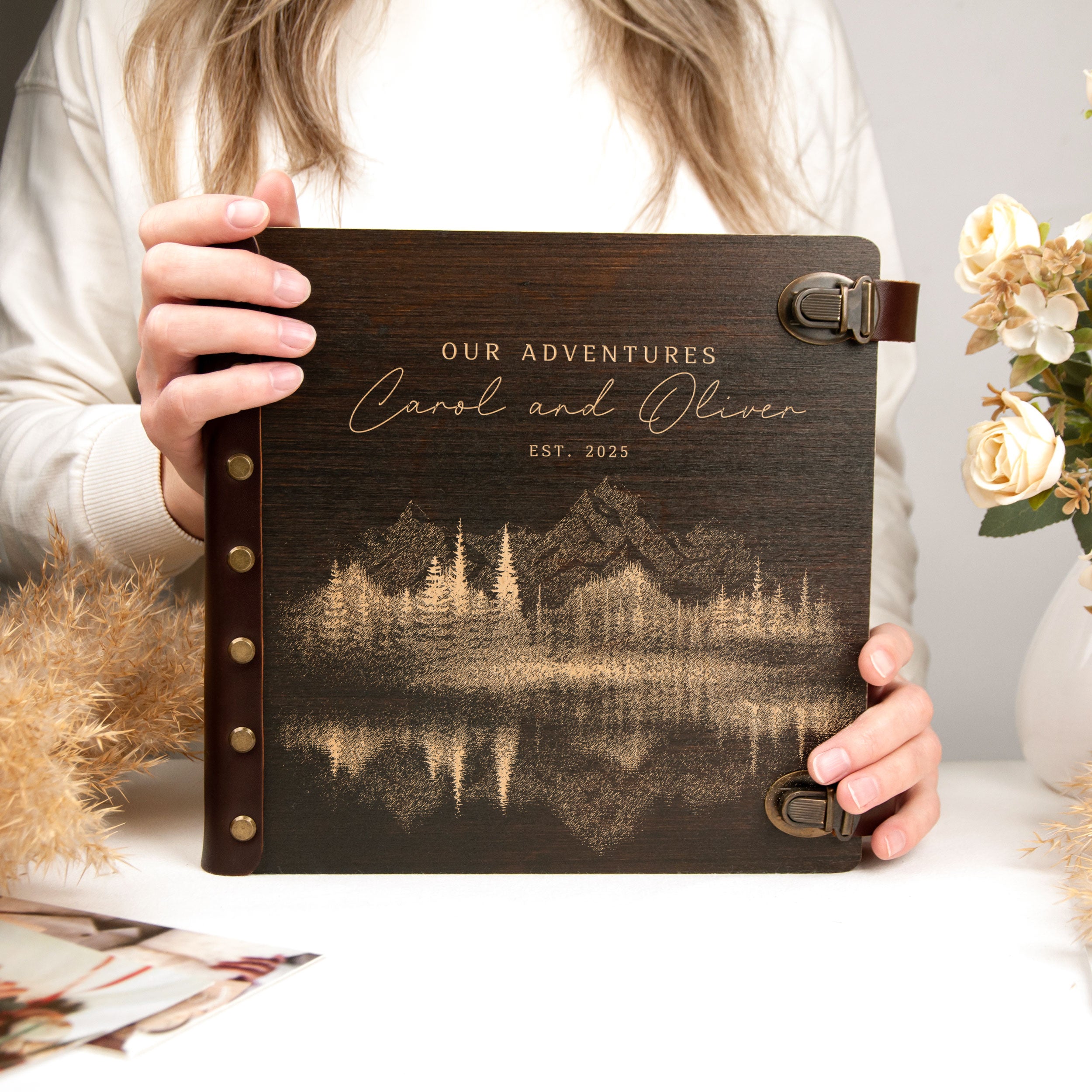 A person is holding a wooden photo album with a landscape scene printed on the cover.