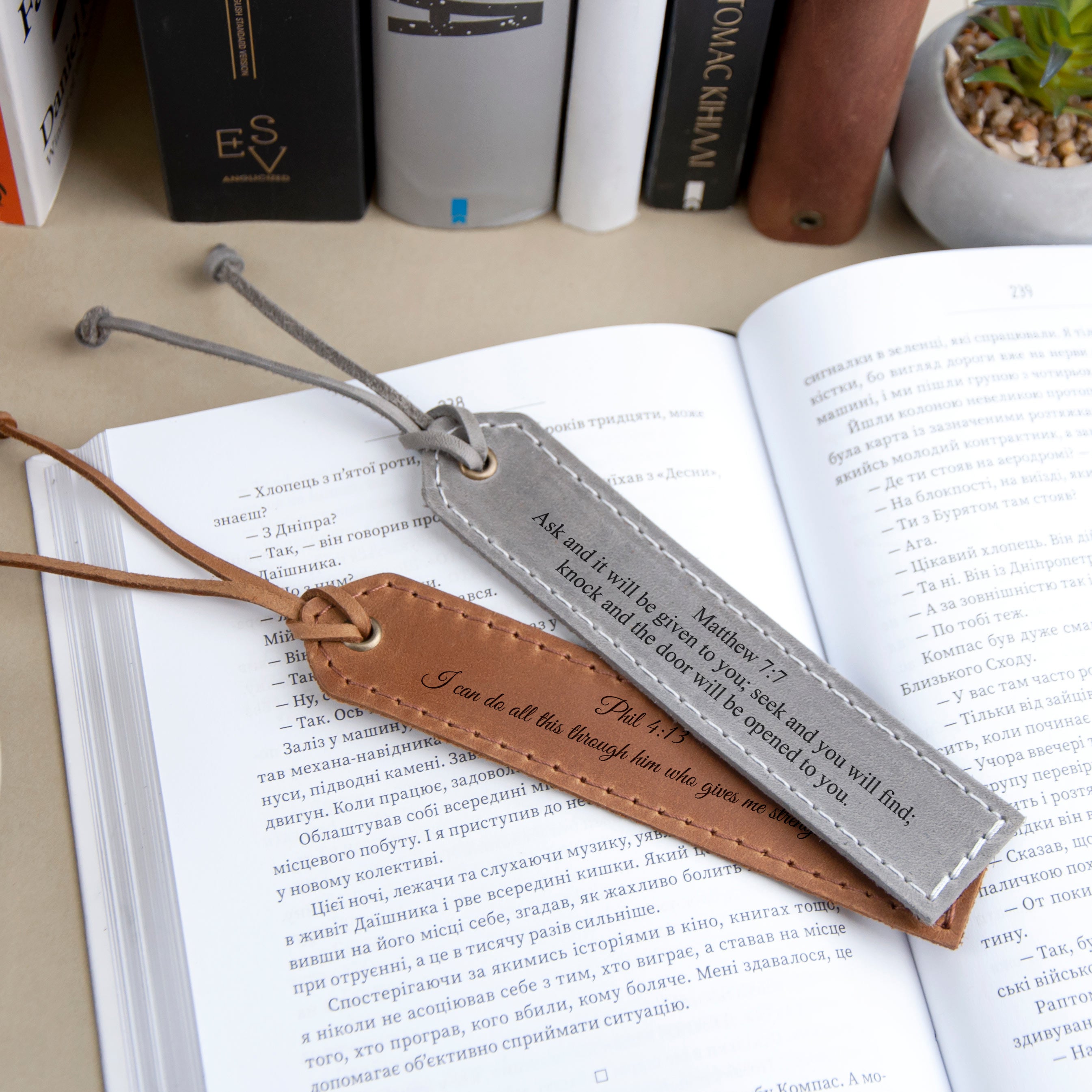 a pair of leather bookmarks resting on an open book, with a black and white book visible in the background.
