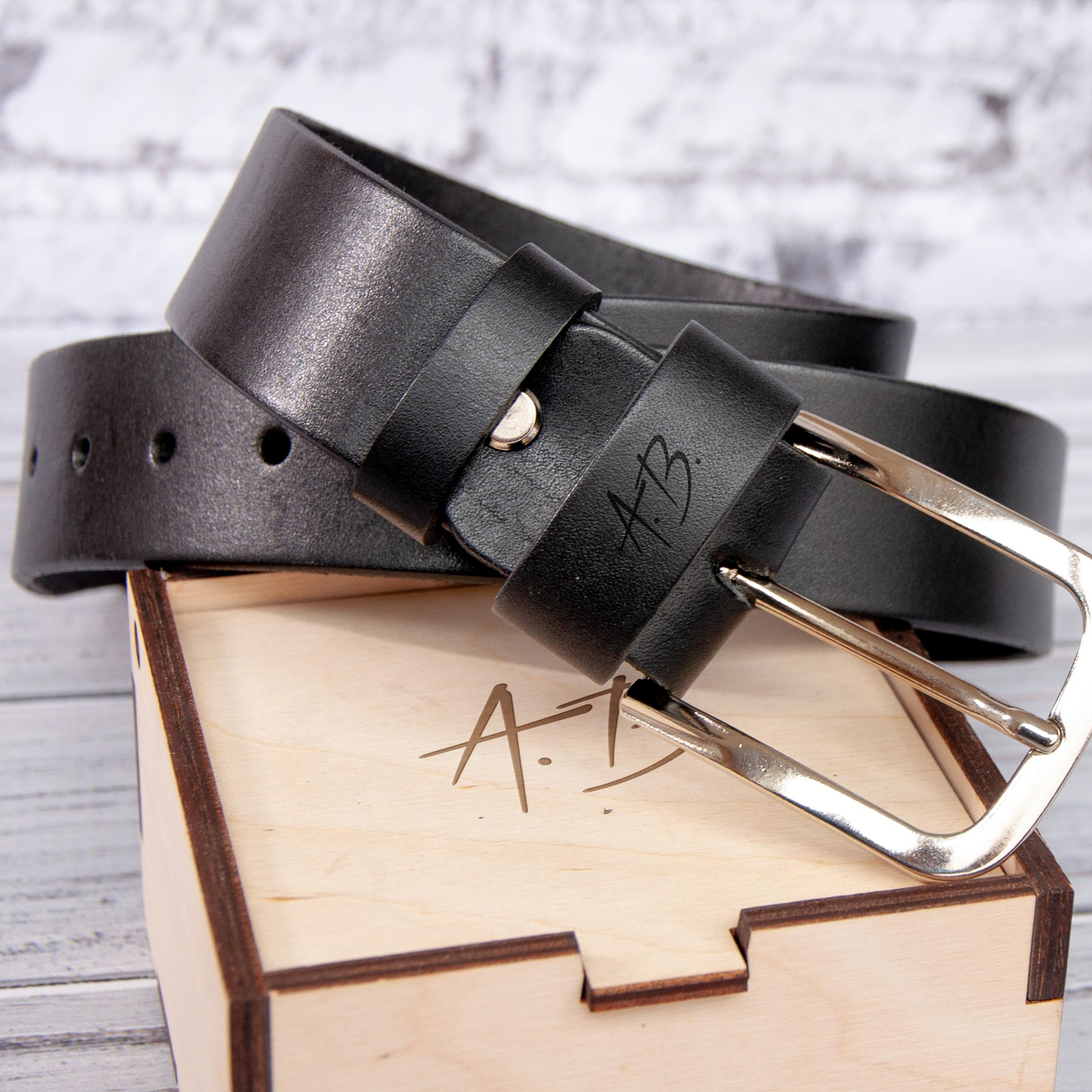 A black leather belt with a metal buckle is placed on top of a wooden box with a carved design.