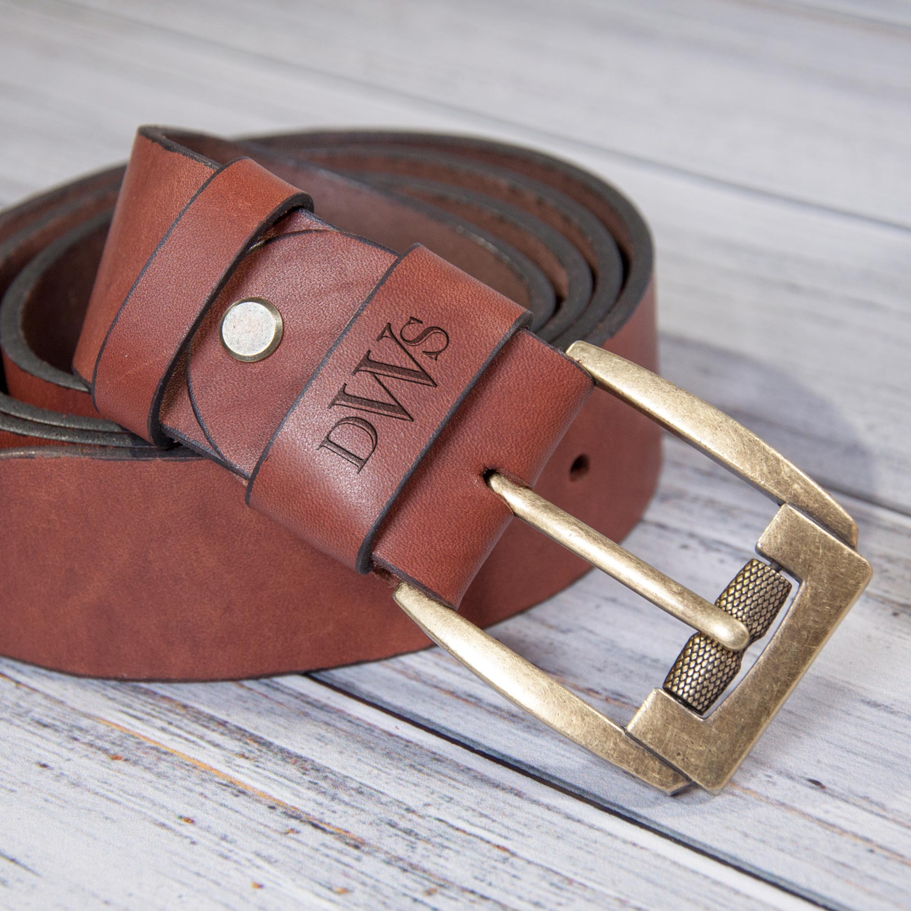 A brown leather belt with a gold buckle, featuring the initials "DWS" engraved on it.