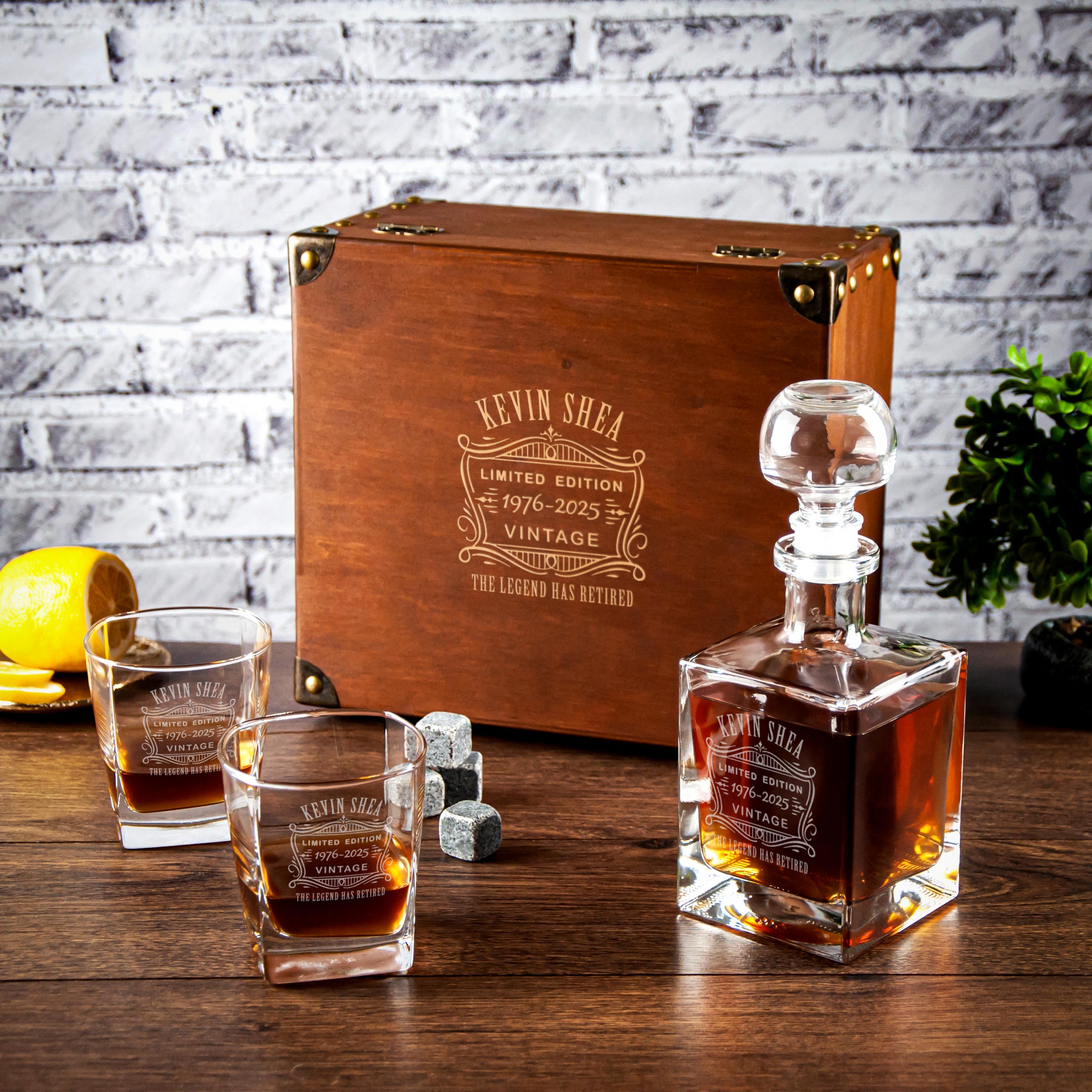a limited edition Kevin Shea vintage decanter and two glasses, all placed on a wooden surface against a brick wall background.