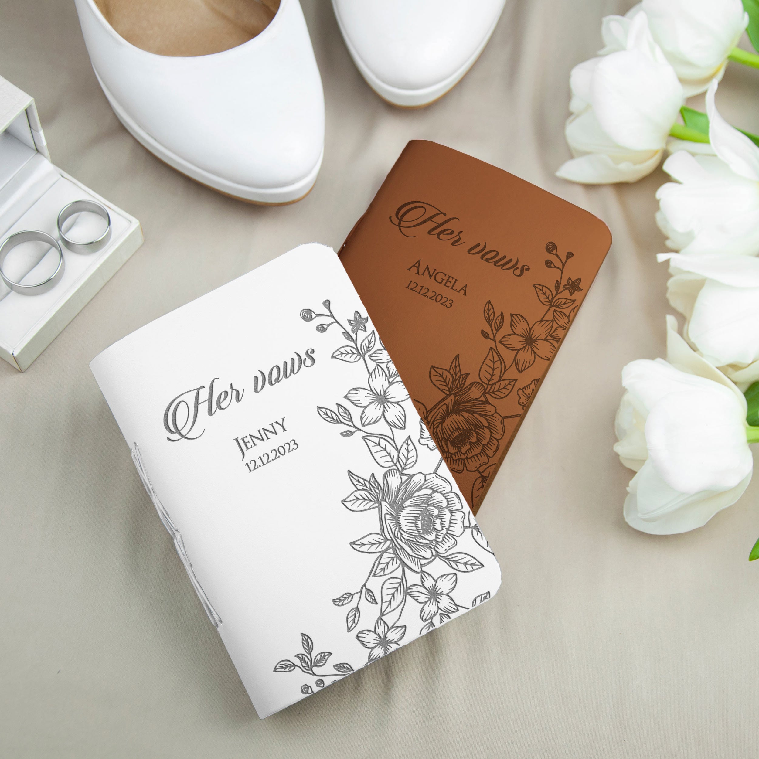a pair of personalized wedding vows books, a pair of white shoes, and a bouquet of white roses, all arranged on a table.