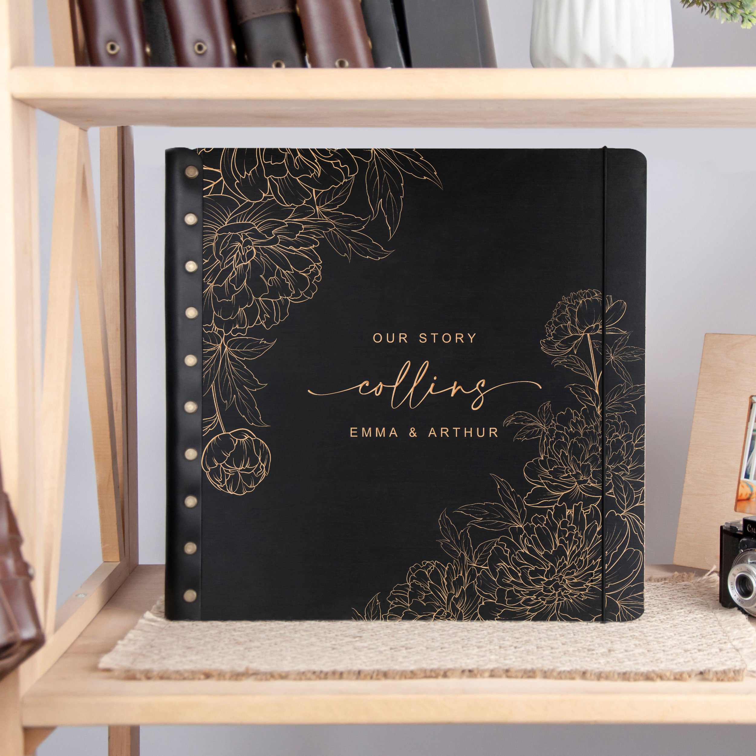 A black photo album with gold floral designs and text, placed on a wooden shelf.