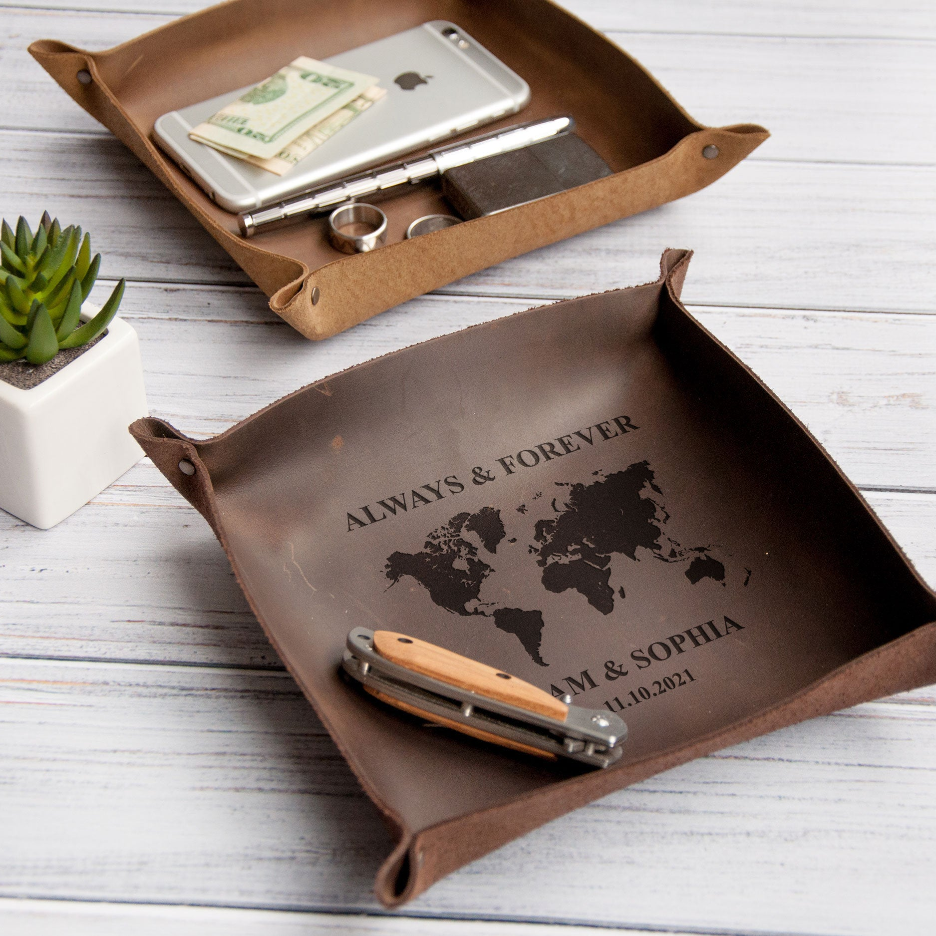 a brown leather tray with a world map design, containing various personal items such as a smartphone, a pen, and a pair of scissors.
