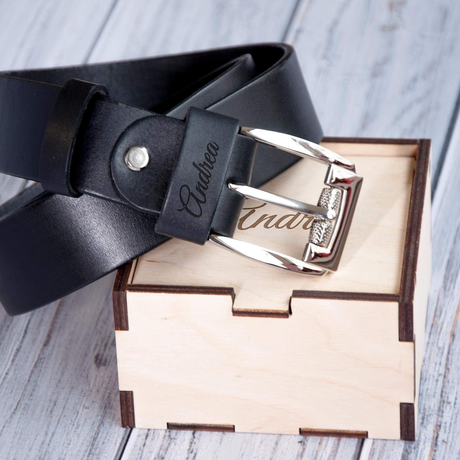 A black leather belt with a silver buckle is placed on top of a wooden box.