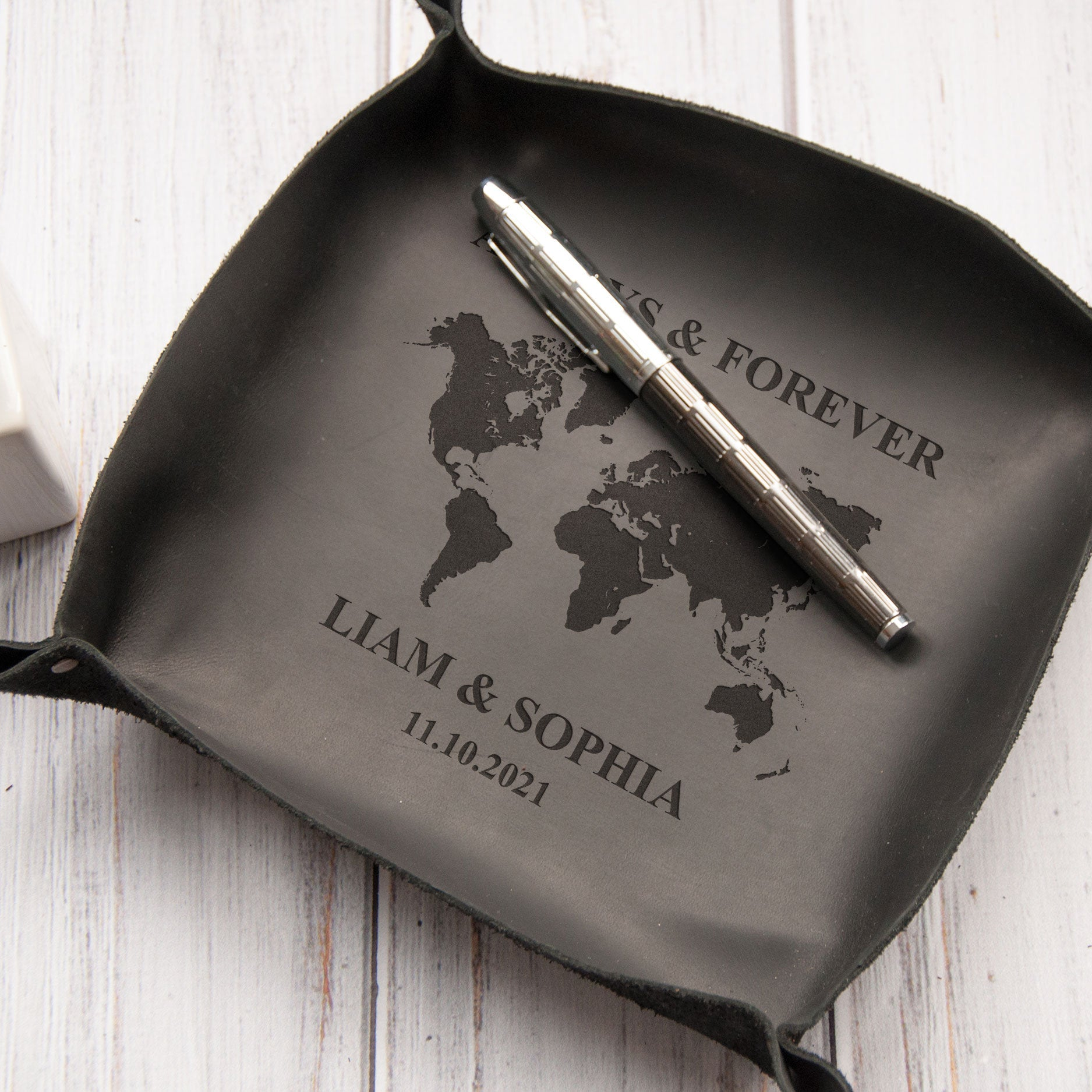 A black leather tray with a world map design and the text "Liam & Sophia 11.10.2021" printed on it.